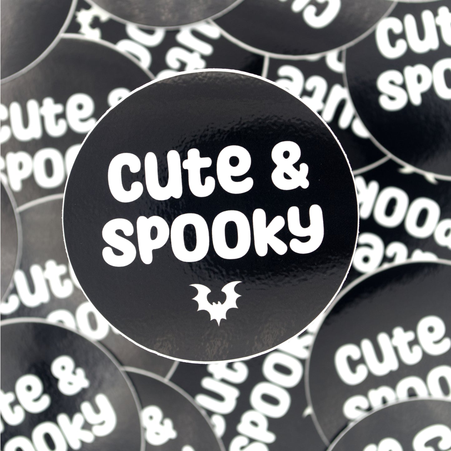 A pile of black stickers with a small bat and the words "cute and spooky" in white ink