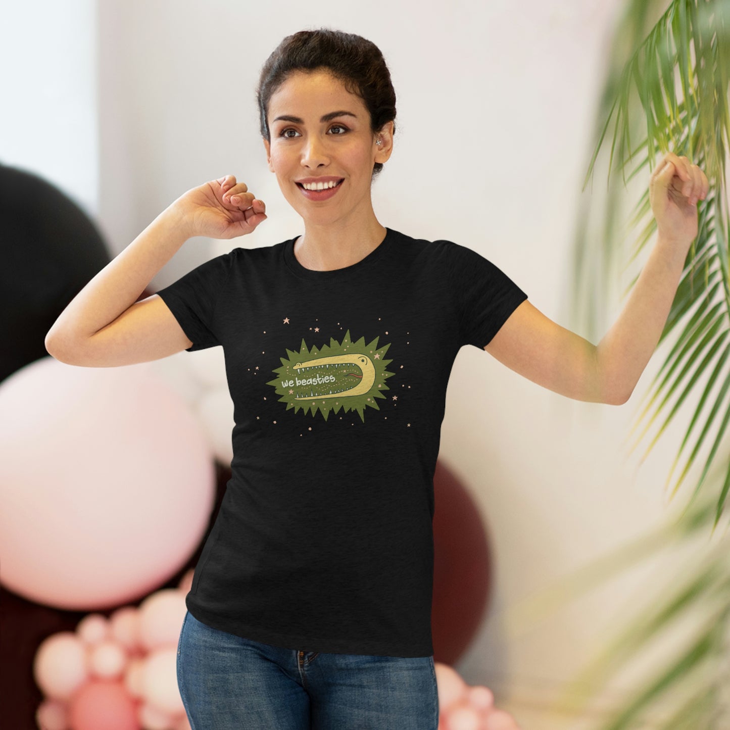 A women with short, dark hair wearing a black t-shirt with the We Beasties logo (a yellow alligator on a green star burst surround by pink stars and the words "We Beasties" in the alligator's mouth.)