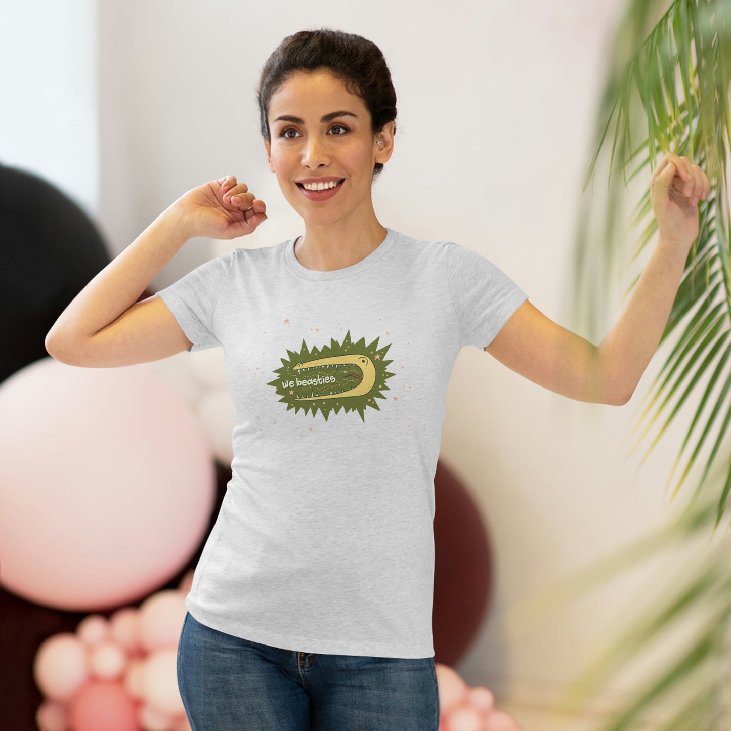 A woman with short dark hair wearing a varigated gray t-shirt with the We Beasties logo (a yellow alligator on a green star burst surround by pink stars and the words "We Beasties" in the alligator's mouth.)
