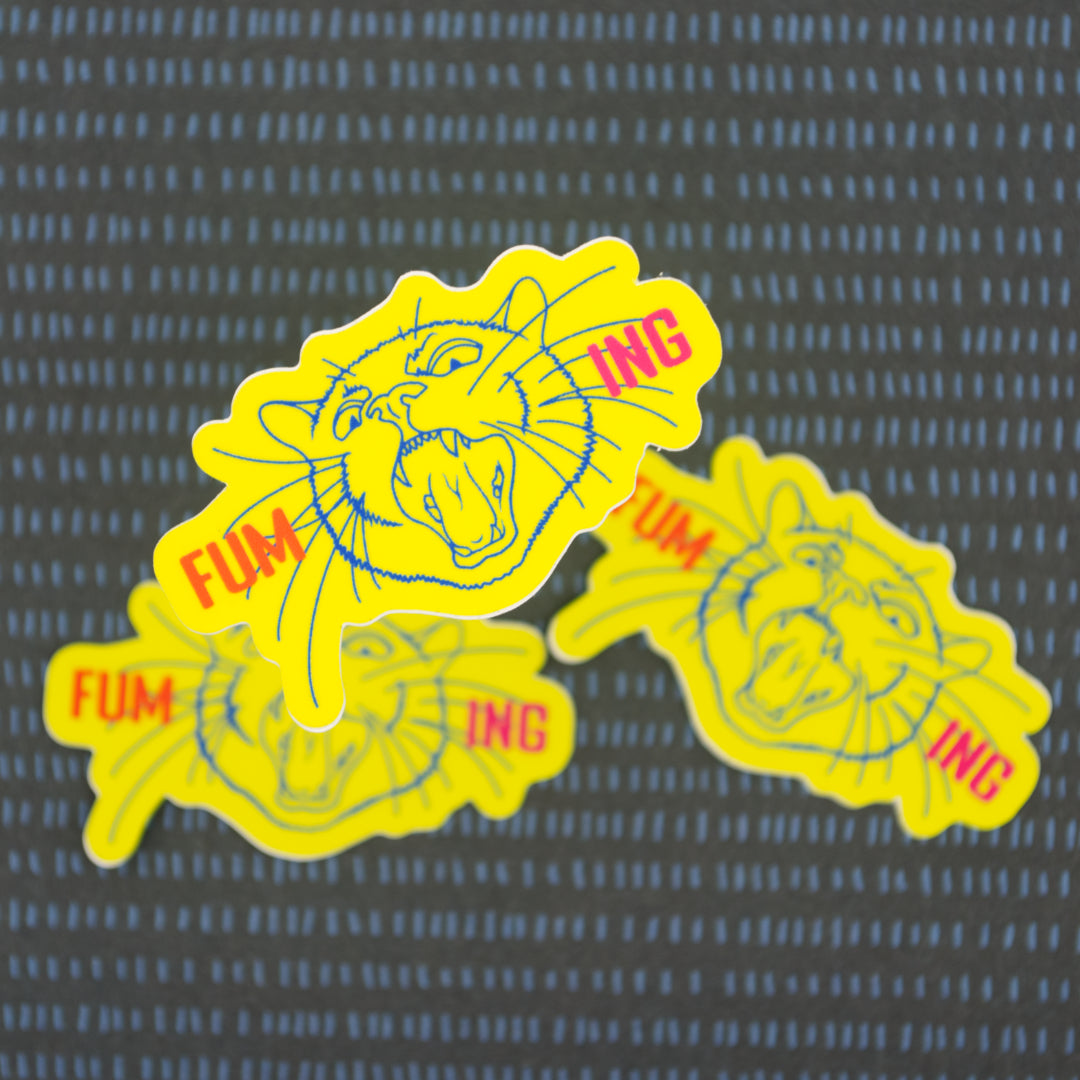A neon yellow sticker with the word fuming broken into two on either side of a screaming cat head.