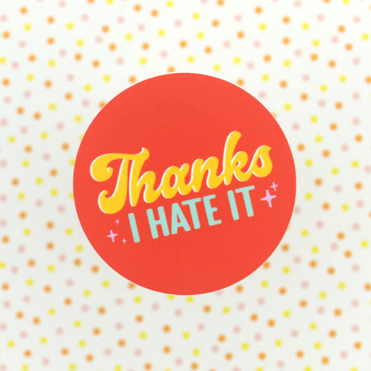 An orange sticker with the words "Thanks I Hate It" in yellow and blue letters, and with purple stars around them
