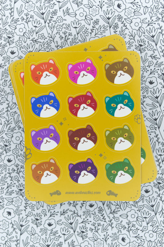 A stack of yellow sticker sheets with illustrations of cat heads in different colors against a black and white flower background.