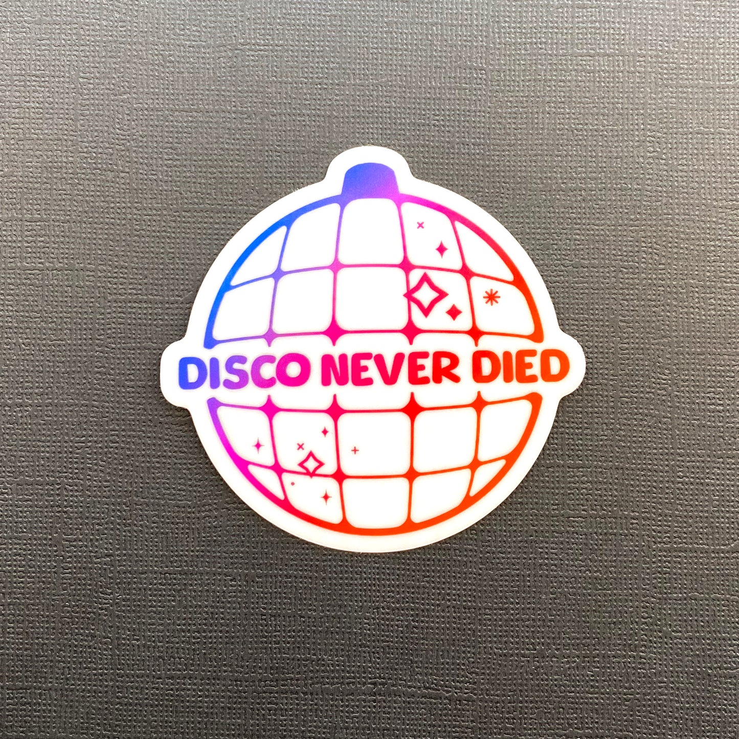A single, holographic "Disco Never Died" sticker on a black background. The sticker features a purple to pink to orange gradient.