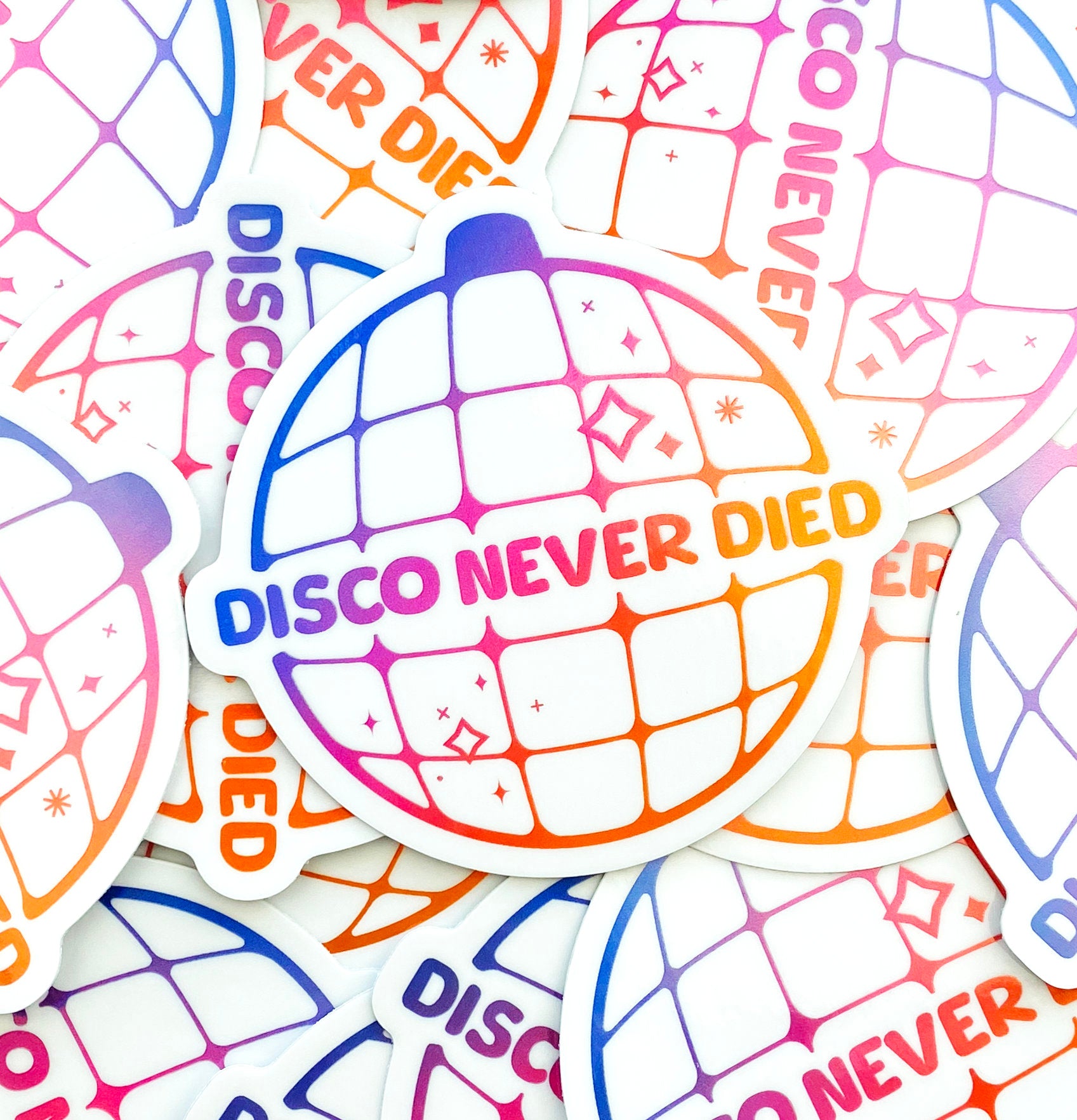 A pile of holographic "Disco Never Died" stickers which feature a purple to pink to orange gradient..