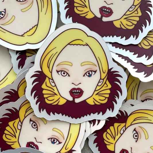 A pile of stickers featuring an illustration of Lady Gaga's head as she appears in American Horror Story. She has a tear in one eye, vampire fangs, red lipstick, and a red fur collar. Her hair is coiffed in a retro 1940's inspired style.