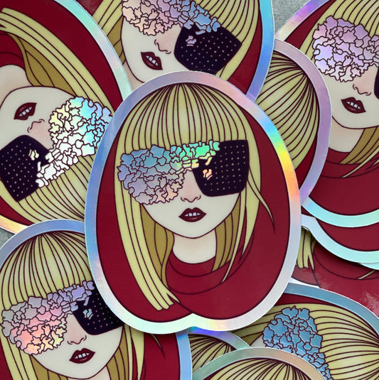A pile of illustrated stickers of Lady Gaga wearing a red hood and black and irridescent glasses