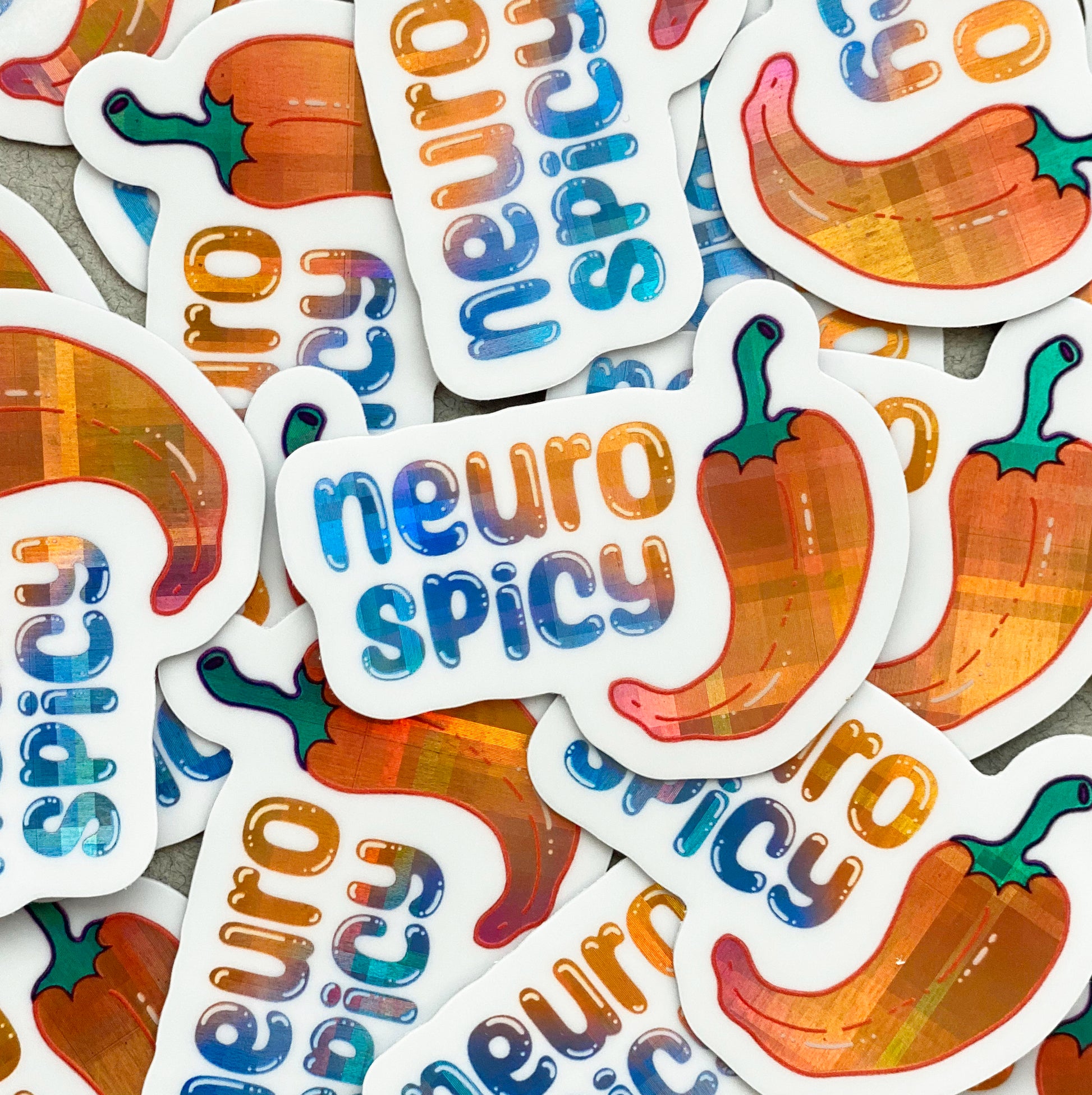 A pile of holographic vinyl stickers with an illustration of a pepper and the words "neuro spicy". The holographic material is a blue to purple to orange gradient pattern with a plaid effect.