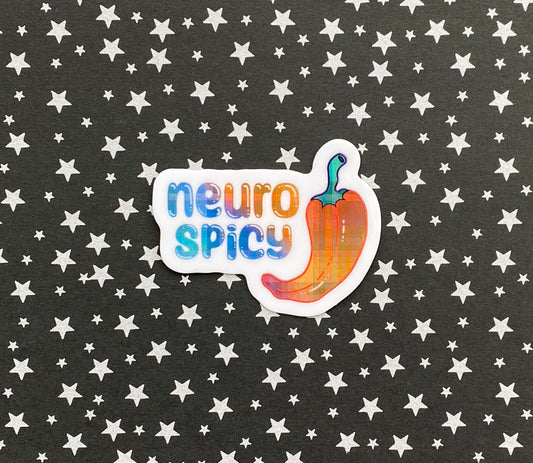 A holographic vinyl sticker with an illustration of a pepper and the words "neuro spicy". The holographic material is a blue to purple to orange gradient pattern with a plaid effect. The sticker sits on top of a black paper background scattered with silver stars.