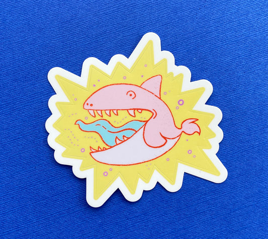 A child-like illustration of a coral pink orca with sharp teeth. It's surrounded by pink bubbles and sits on a yellow star burst. The sticker is kiss cut.