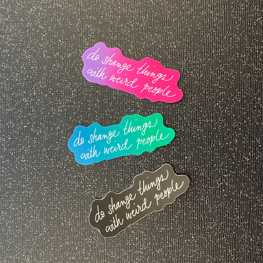 Three metallic stickers that say "do strange things with weird people" on a variety of backgrounds. The stickers sit on black glitter paper.